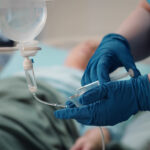 Cropped shot of unrecognizable person in latex gloves injecting poison in drip tube killing senior woman patient in hospital ward. Criminal poisoning old ill female in clinic